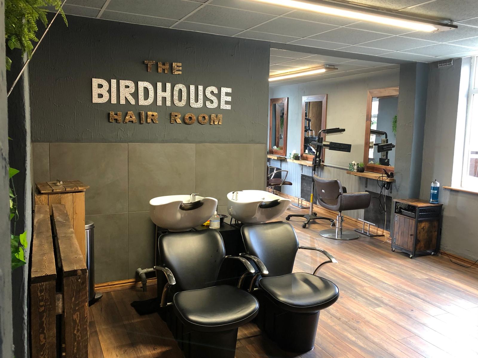 The Birdhouse hair room, aninterior image of the salon with its warm wooden decor and a large sign over the wash area reading 'The Birdhouse hair room.